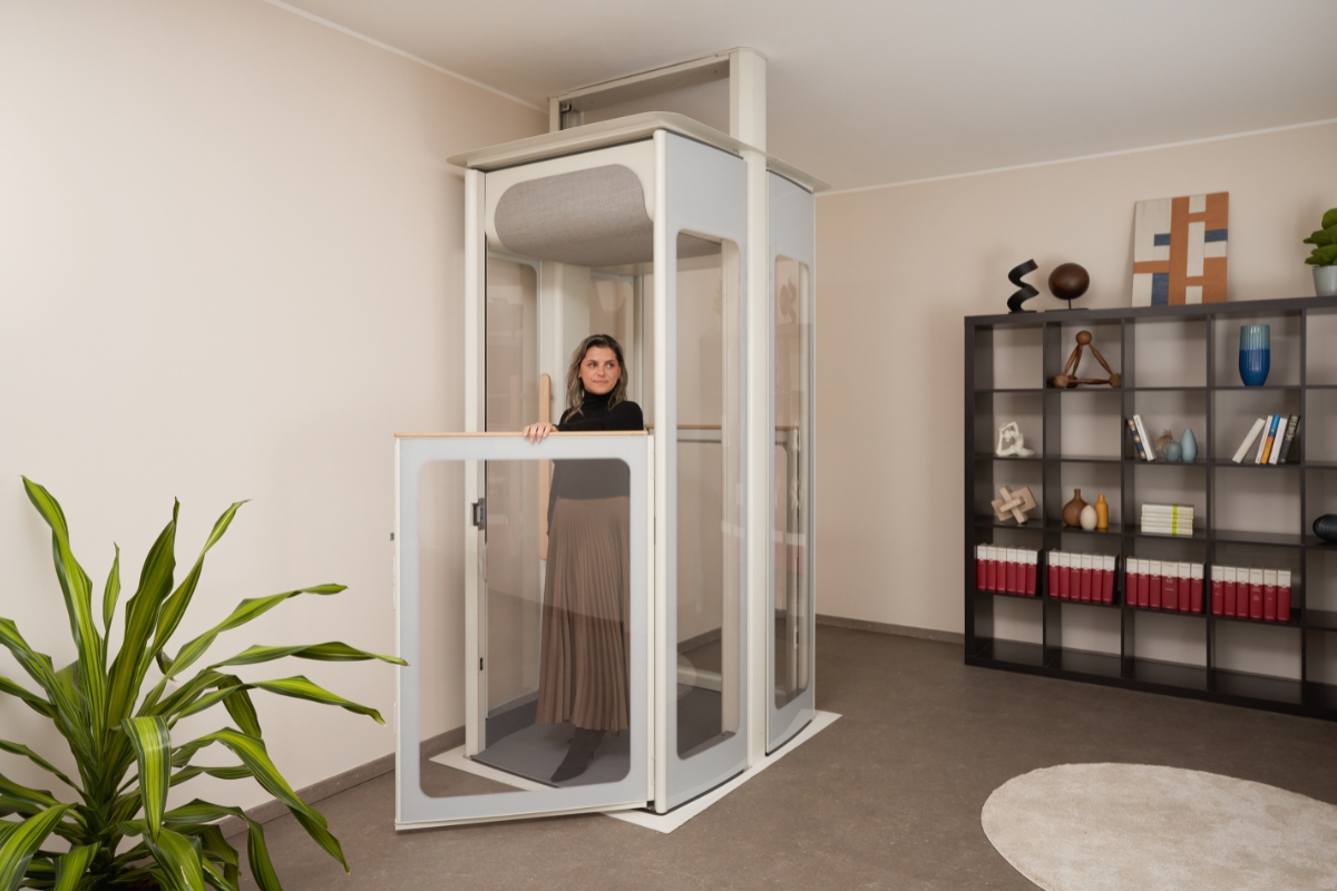 Žena uvnitř domácího výtahu Stannah Uplifts. Otevřené dveře jsou průhledné a výtah zabírá jen minimální prostor.