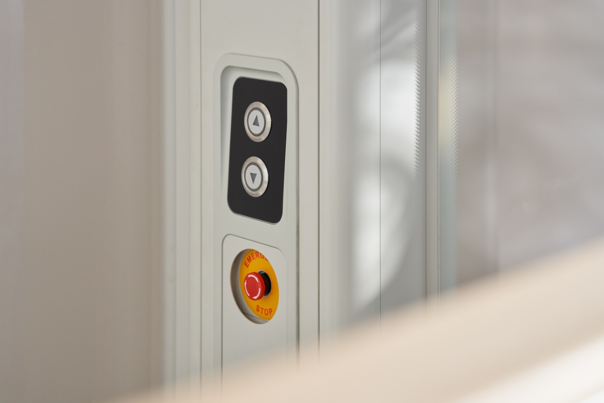 Pohled zblízka na ovládací panel domácího výtahu Stannah Uplifts s tlačítky pro jízdu nahoru a dolů. Nechybí ani červené tlačítko pro nouzové zastavení zajišťující bezpečný provoz. 