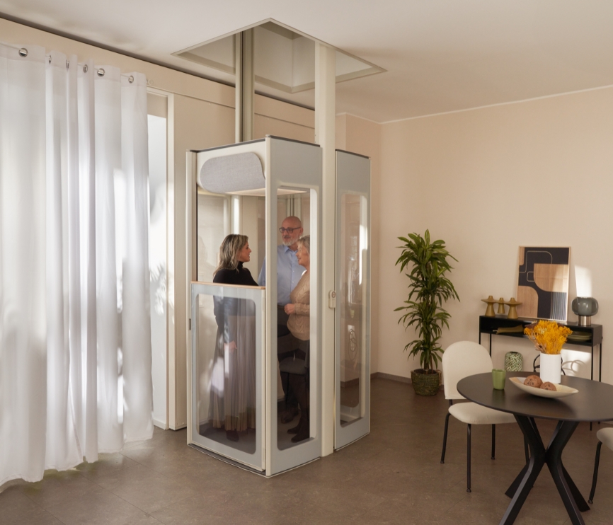 Tři dospělí stojící uvnitř domácího výtahu s průhlednými panely v moderní jídelně a obývacím pokoji.