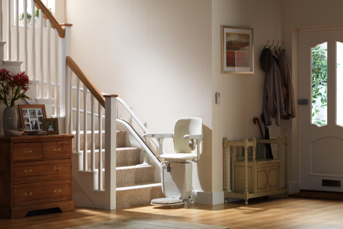 Béžový schodišťový výtah s zakřivenou kolejnicí nainstalovaný podél schodiště ve světlé chodbě.